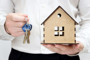 Man holding keys and a miniature wooden house model in hands. Get the keys day concept.