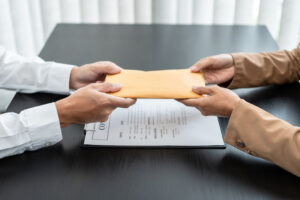 A person hands an envelope across a desk to another person