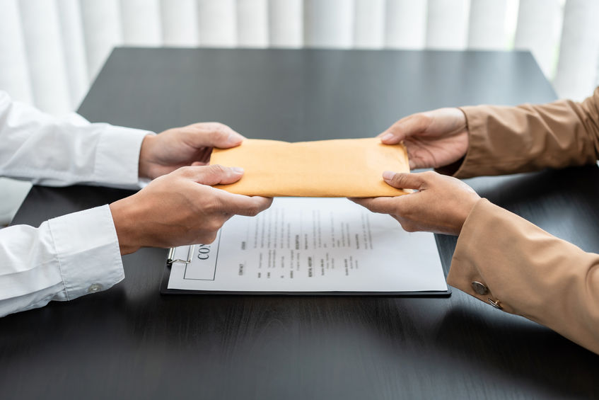 A person hands an envelope across a desk to another person